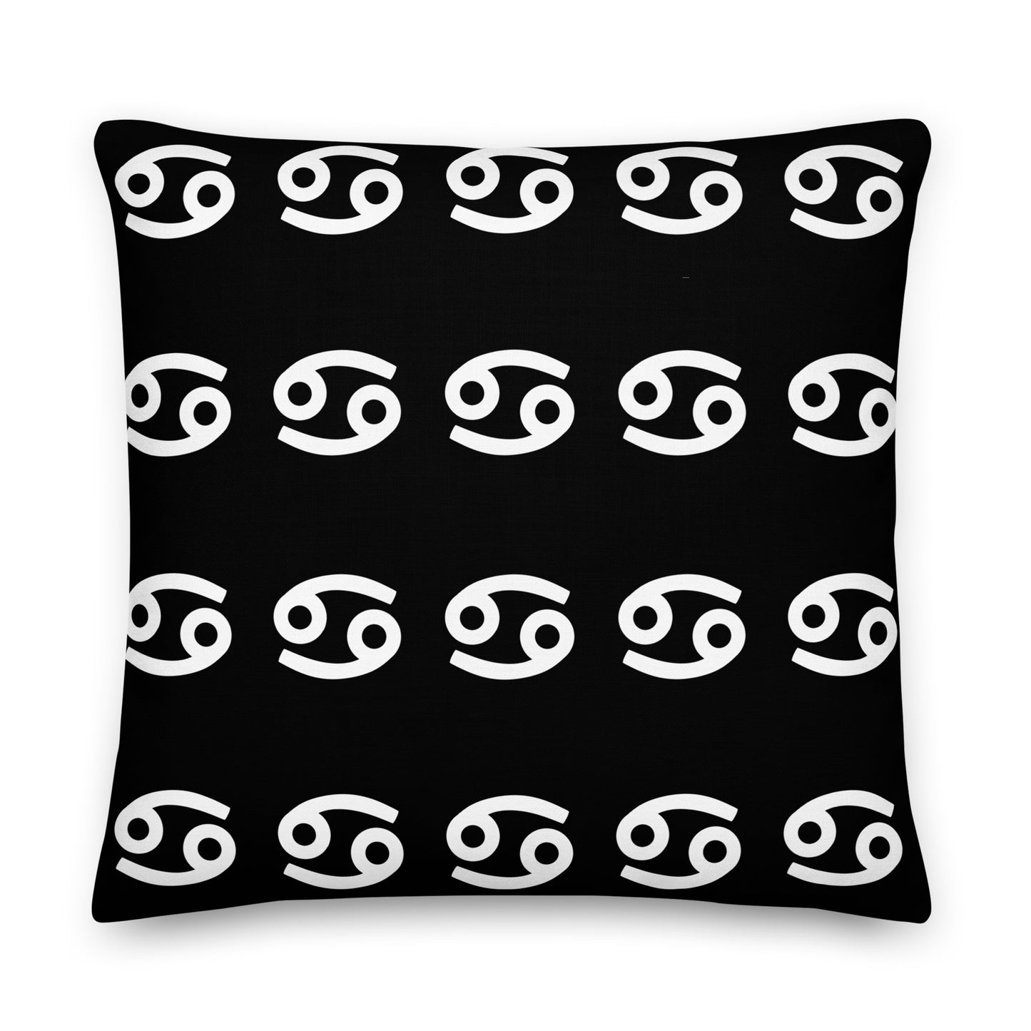 A luxury black square pillow with a pattern of white cancerian symbols, placed on a fluffy white surface.