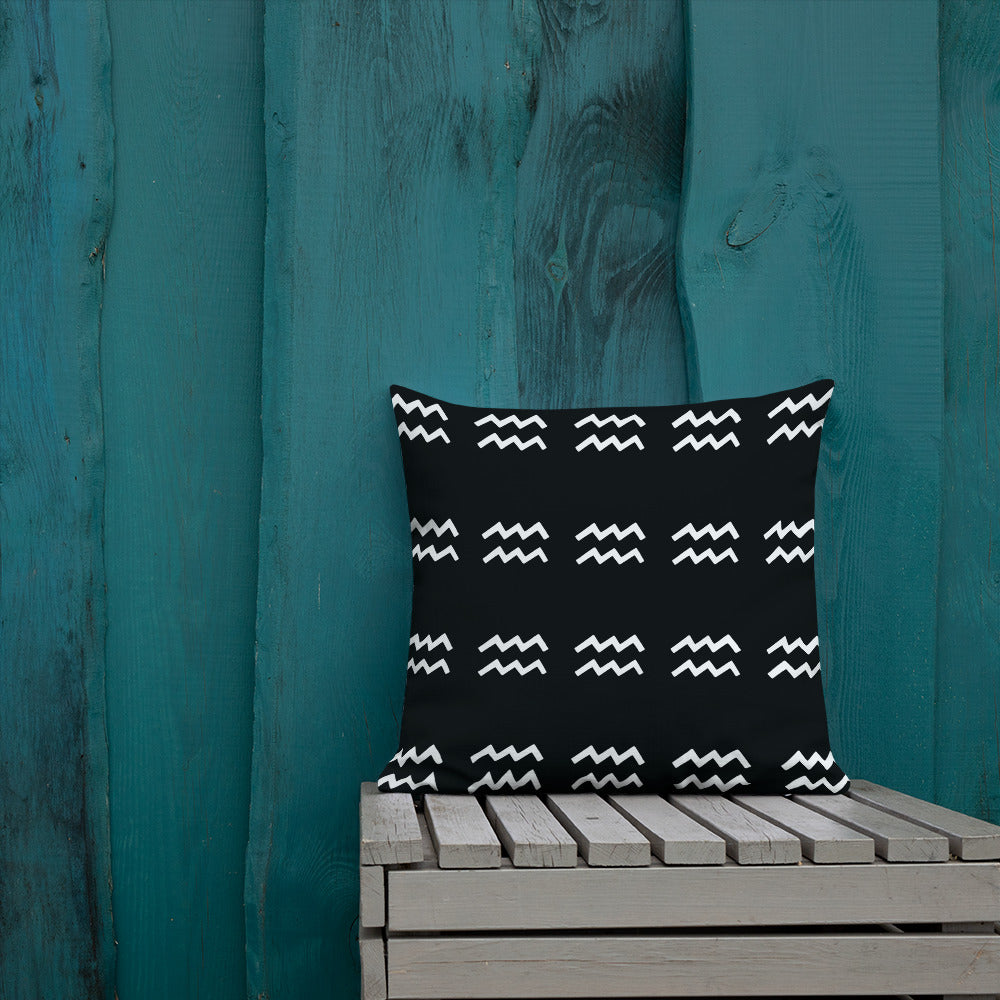 A black cushion with a geometric pattern, placed on a wooden bench against a blue wooden wall.