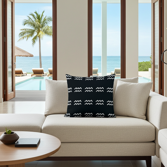 Beige sofa with a black pillow featuring white Aquarius patterns, set against a backdrop of a pool and ocean view.