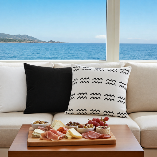 Beige sofa with a black aquarius patterned white pillow, wooden coffee table with appetizers, and ocean view.