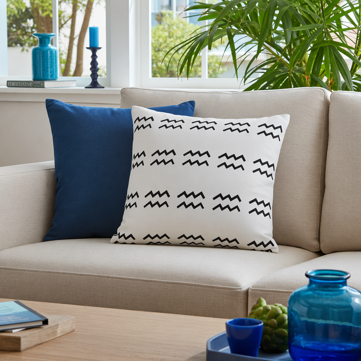 Beige sofa with an aquarius patterned white pillow, surrounded by decorative items.