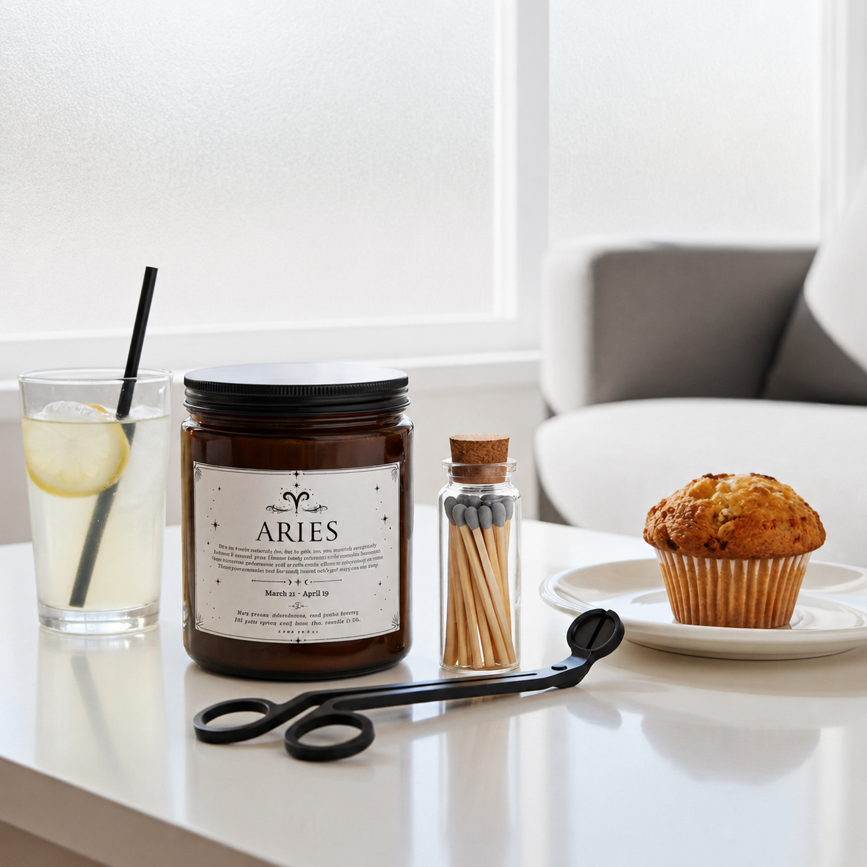 Candle labeled 'ARIES' on a table with a glass of lemonade, muffin, and matches.