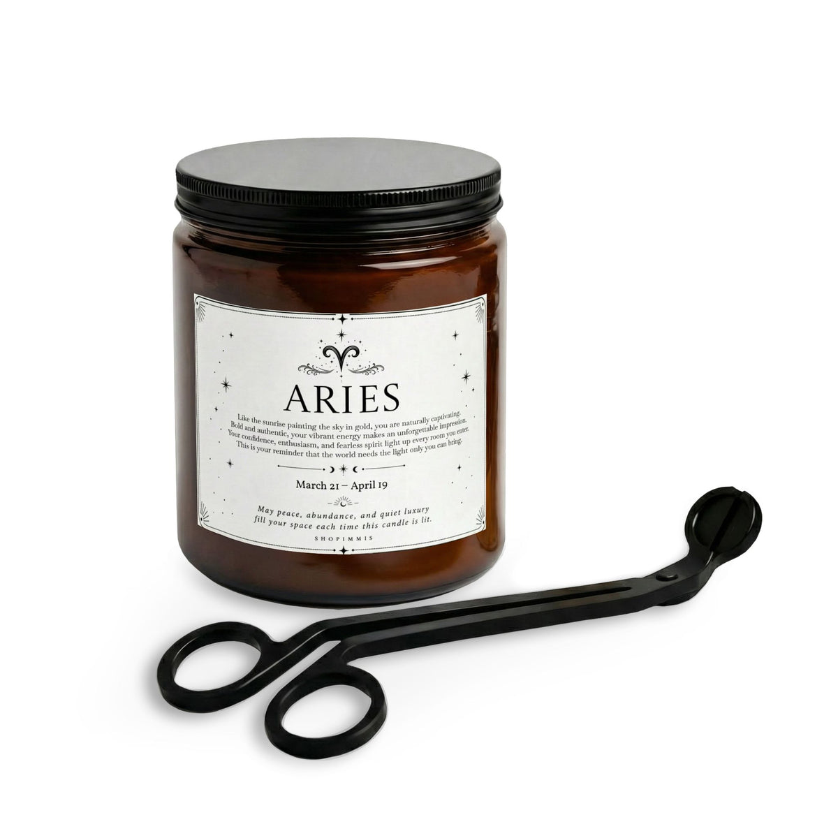 An amber glass jar candle with a black lid and a white label reading 'ARIES', shown with a black metal tongs tool on a clean white background.