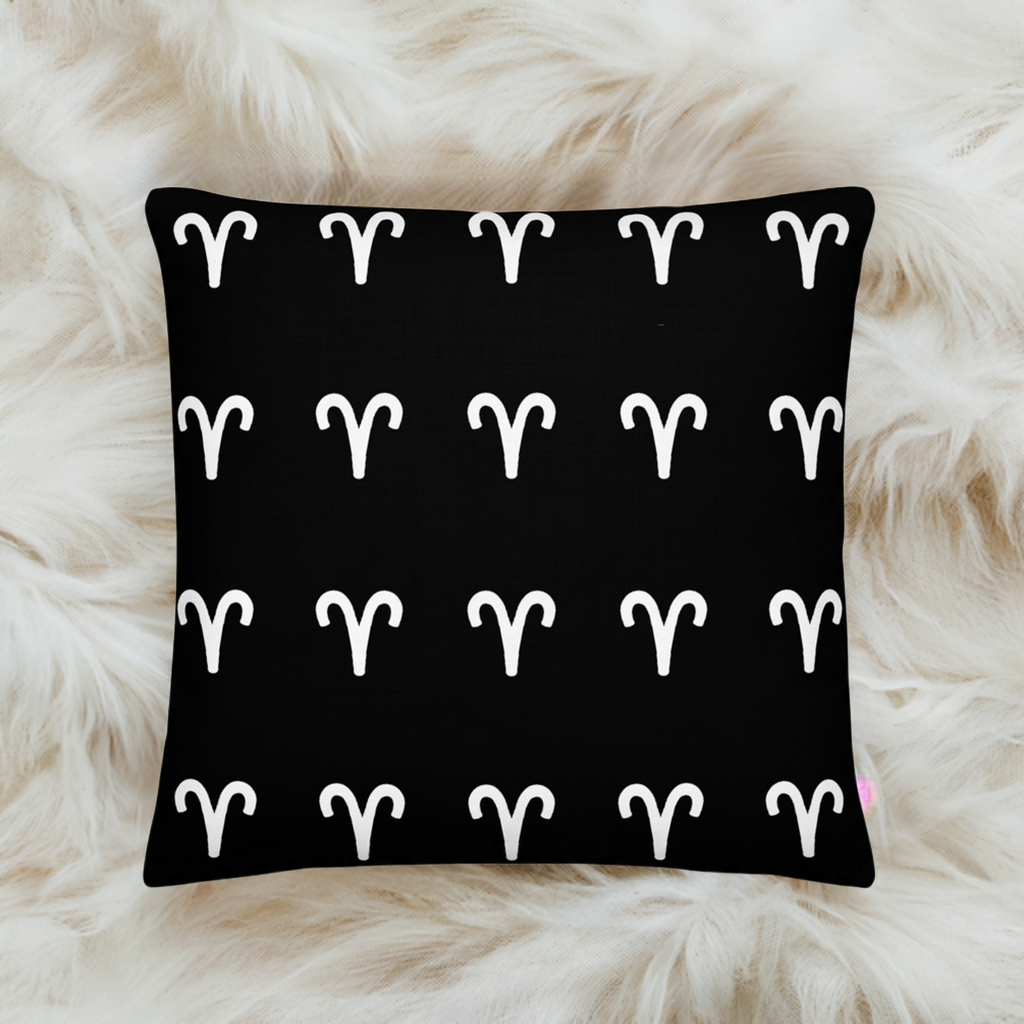 A luxury black pillow with a geometric pattern of white aries symbols, placed on a fluffy white surface.