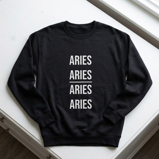 A black crewneck sweatshirt with the word 'ARIES' printed vertically four times in white block letters, separated by a horizontal line, laid flat on a white surface.