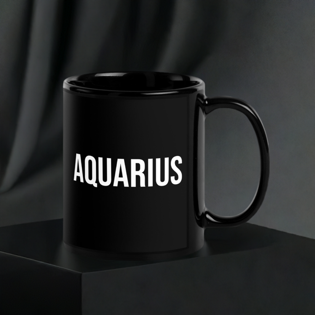 A black ceramic mug with 'Aquarius' and the Aquarius Zodiac Symbol printed on it, placed on a dark surface with a blurred background.