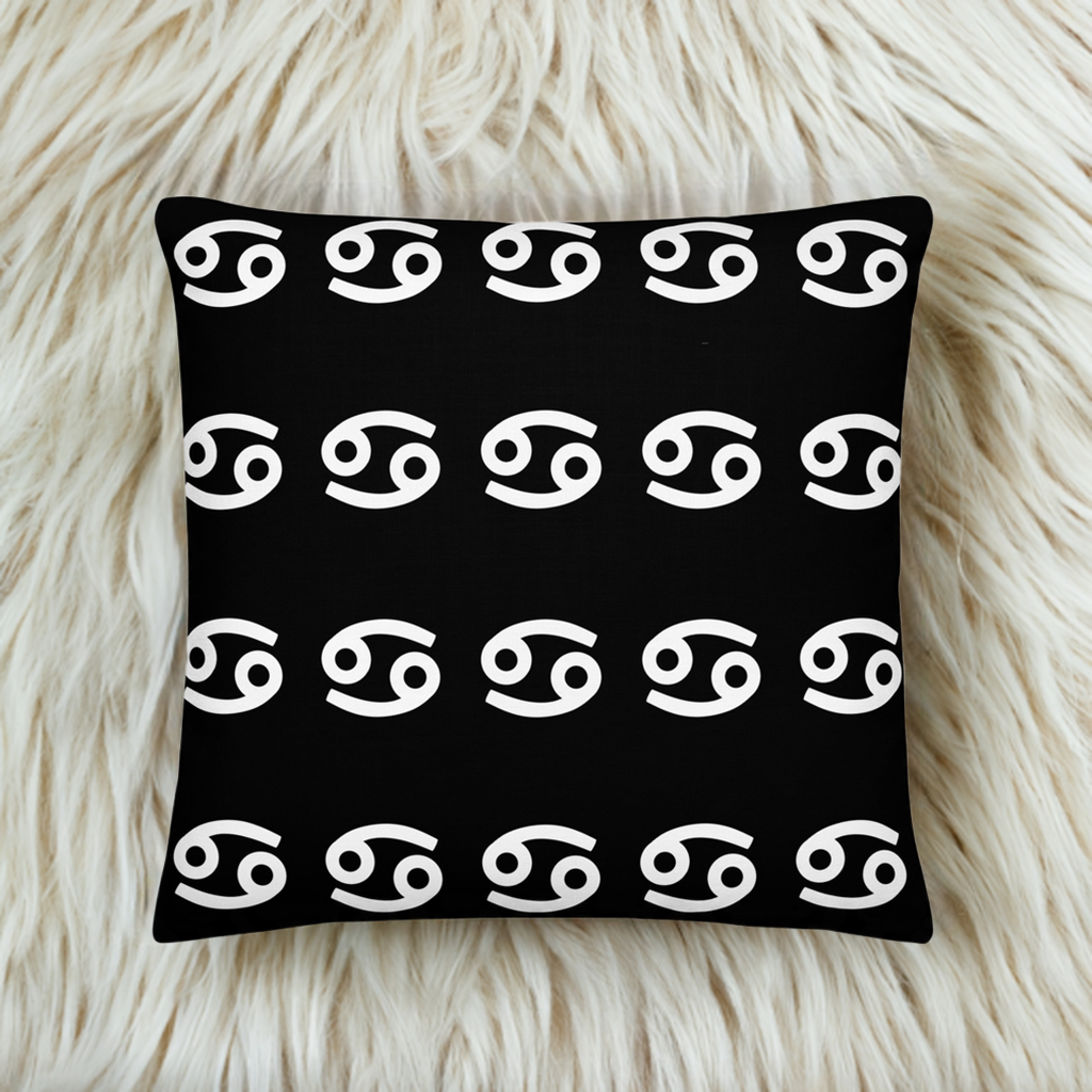 A luxury black square pillow with a pattern of white cancerian symbols, placed on a fluffy white surface.