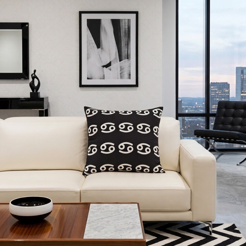 A black throw pillow with a white astrological symbol pattern, styled on a cream leather sofa in a modern living room setting.