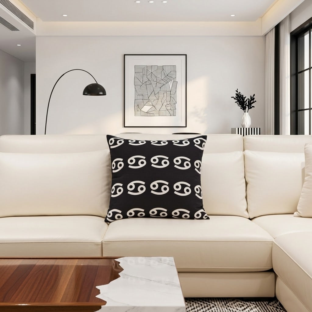 A black throw pillow with a white astrological symbol pattern, styled on a cream-colored sectional sofa in a modern living room setting.