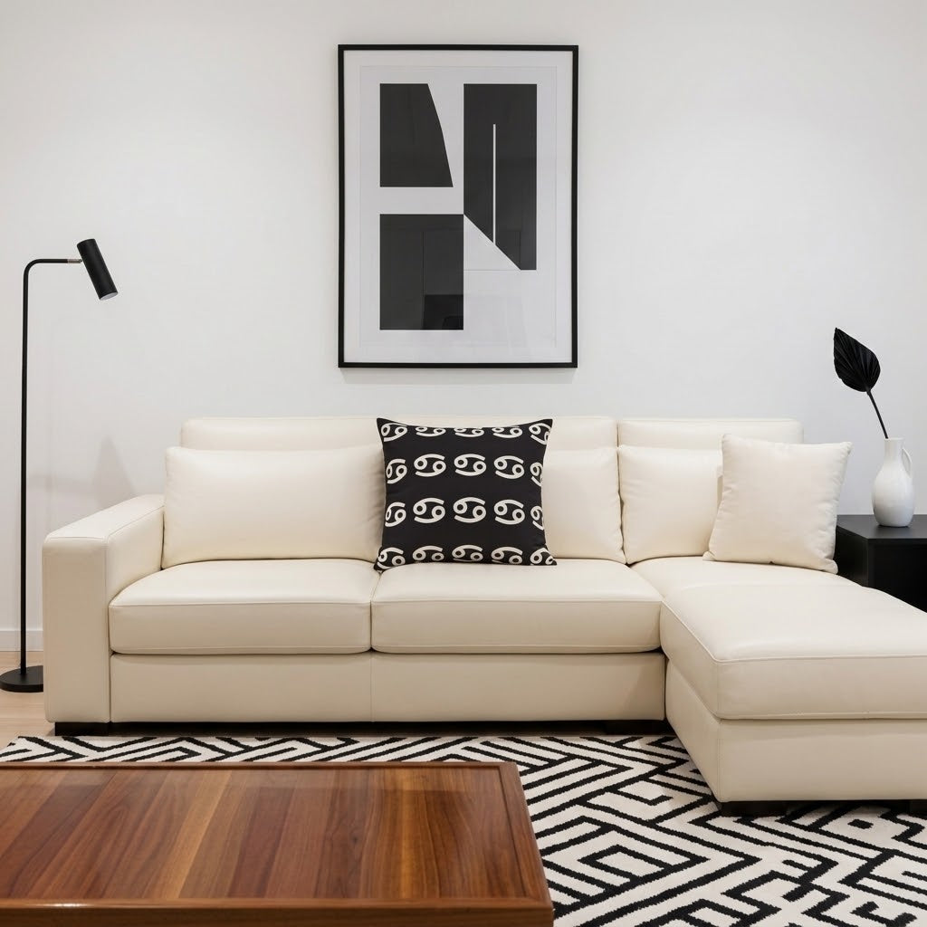 A cream-colored leather sectional sofa with a right-facing chaise lounge, styled in a modern living room with a black and white patterned accent pillow, a black floor lamp, and a black-and-white geometric rug.