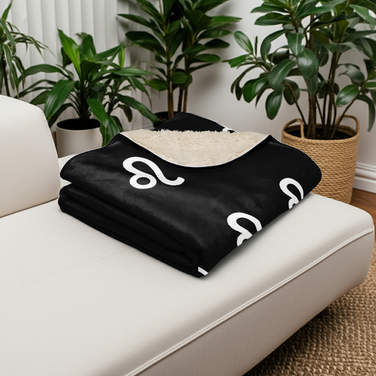 Black blanket with white Leo symbols on a white couch in a room with plants.