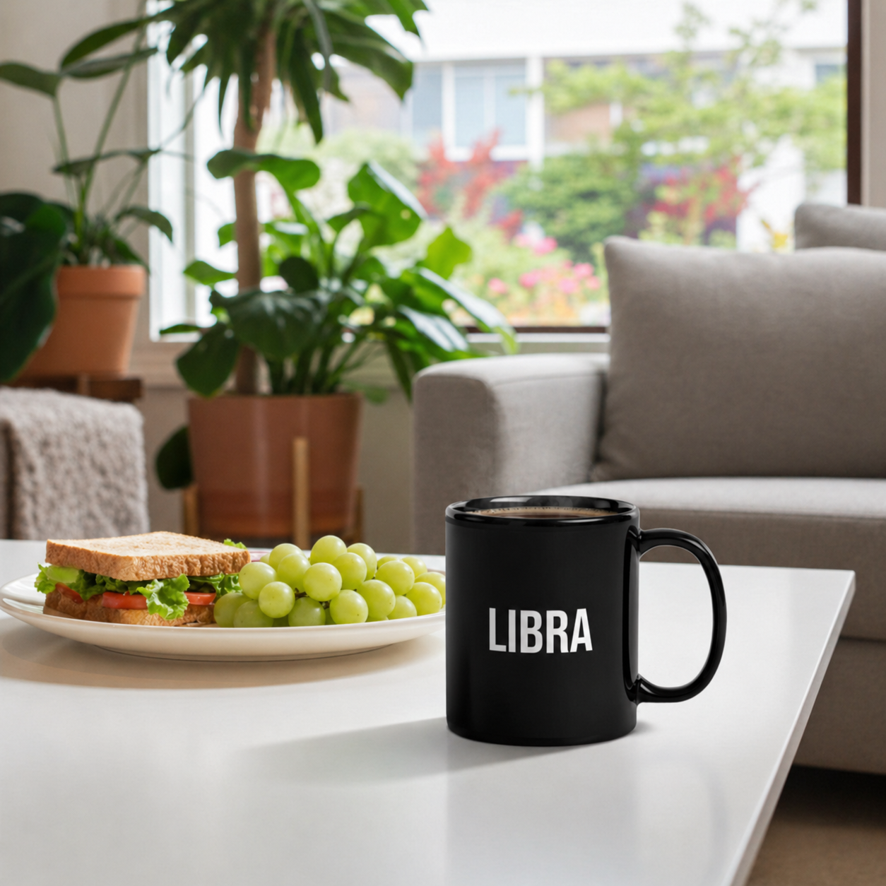 Black mug labeled 'LIBRA' on a table with a sandwich and grapes in a living room.