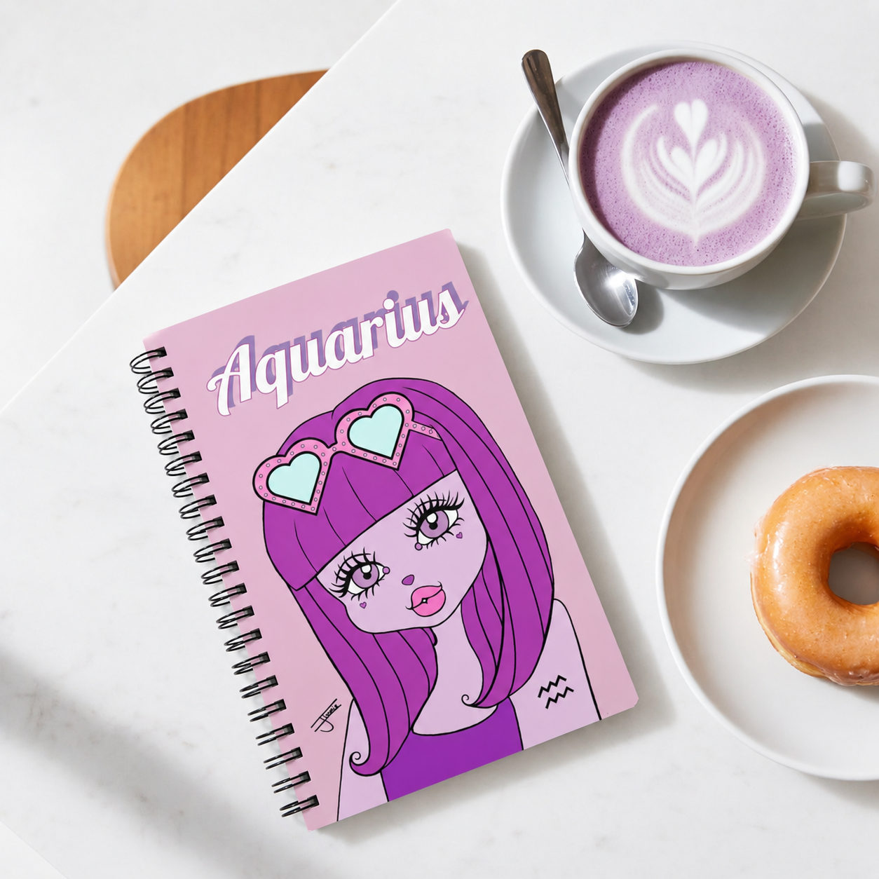 Notebook with Aquarius design, cup of lavender latte, and donut on a white surface