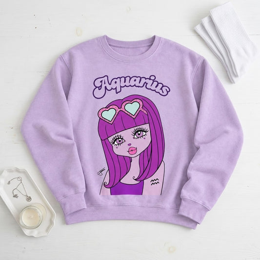 A lavender crewneck sweatshirt featuring a cartoon graphic of an Aquarius girl with purple hair and heart-shaped sunglasses, displayed on a white wooden background with lifestyle props.