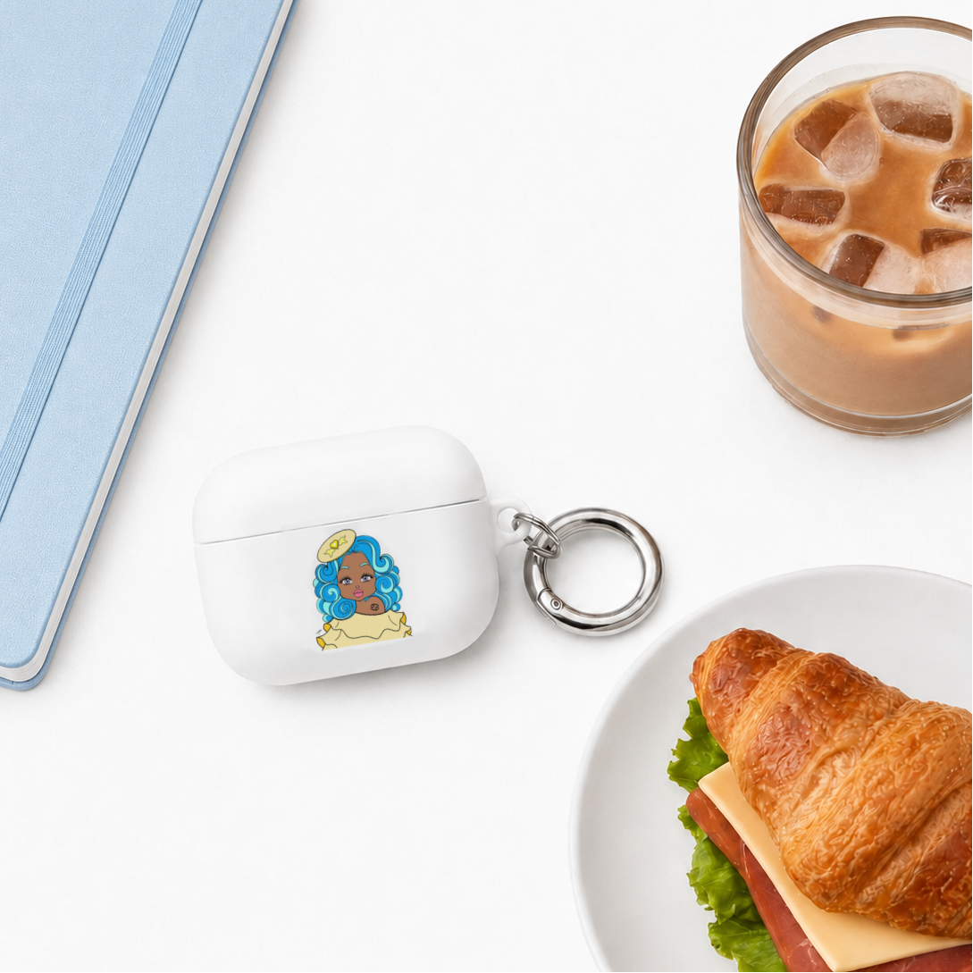 A white AirPods case with a key ring and a cancerian character design, styled on a white surface with a light blue notebook, an iced coffee, and a croissant.
