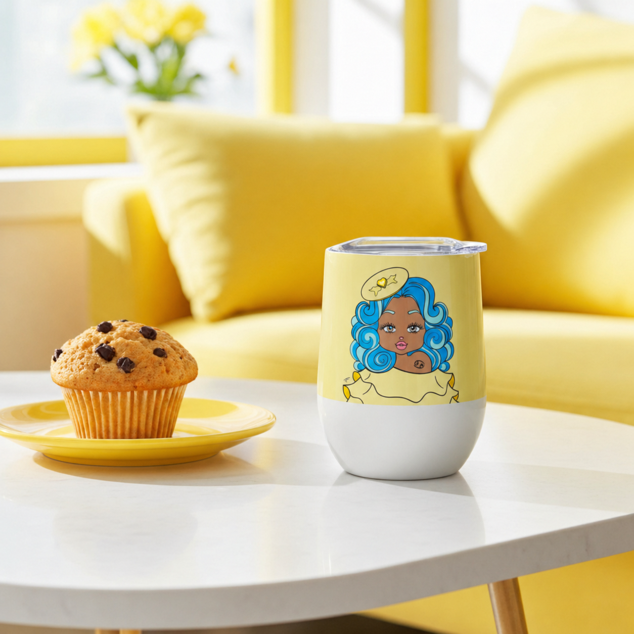 White tumbler with a Cancerian character design on a white table next to a muffin, with a yellow couch and flowers in the background.