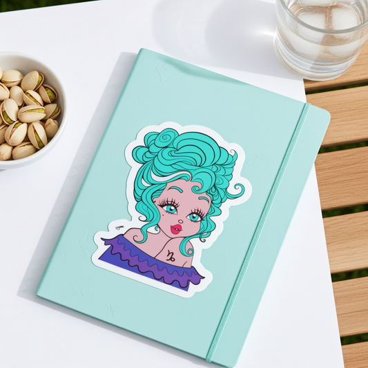 Light blue notebook with a sticker of a capricorn character with teal hair on a white surface.