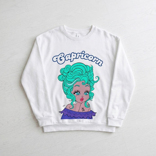 A white crewneck sweatshirt featuring a colorful graphic of a cartoon Capricorn zodiac character with bright teal hair and a purple dress, displayed flat on a light gray wood-textured background.