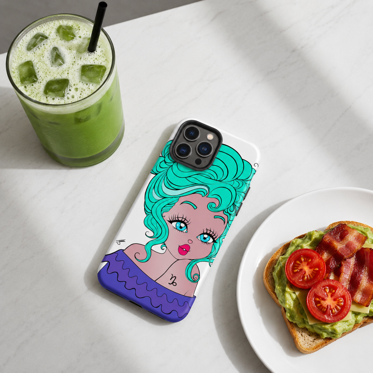 Phone case with a Capricorn character design next to a green drink and avocado toast on a white surface