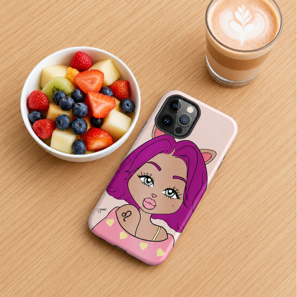 A phone case with a leo character design, shown on a wooden table next to a bowl of fruit and a cup of coffee.