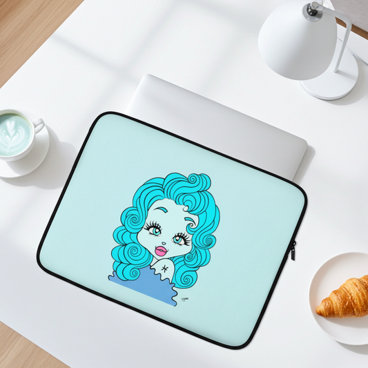 A laptop sleeve with a light blue background and a Pisces character design, shown on a white desk with a laptop, coffee cup, lamp, and croissant.