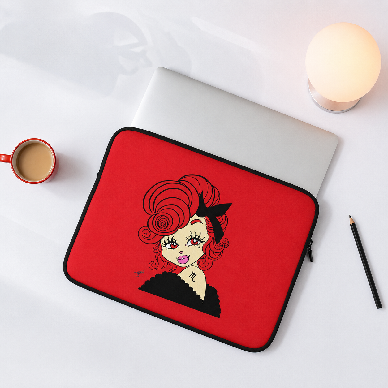 Red laptop sleeve with a scorpio character design on a white surface with a cup and pencil.