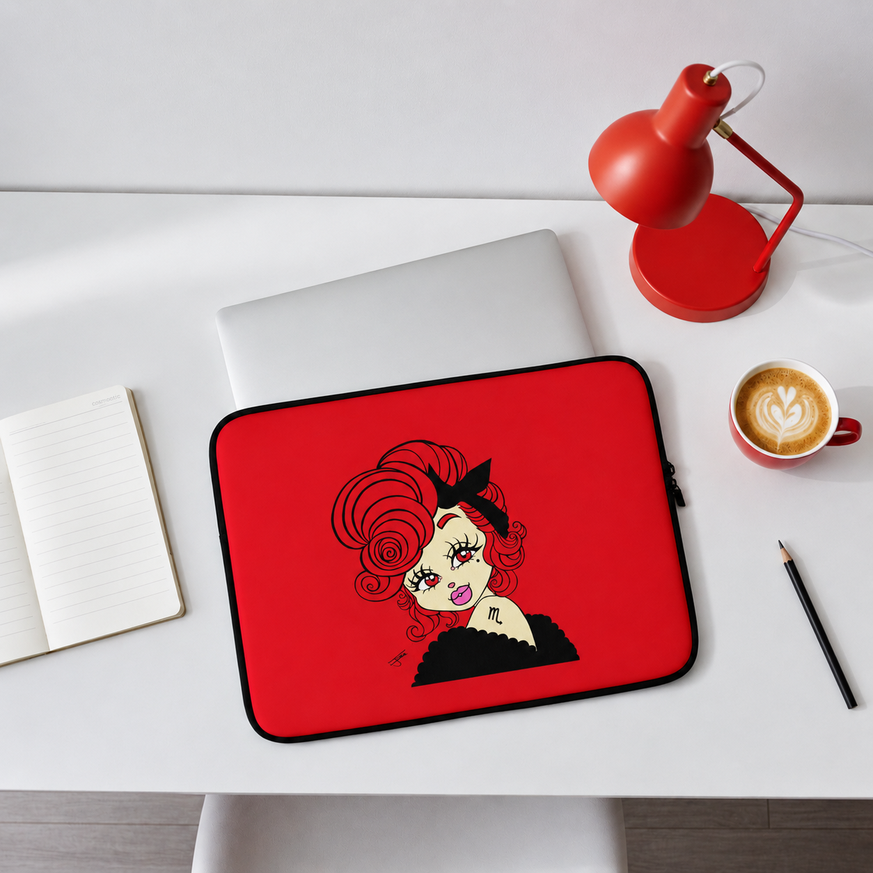 Red laptop sleeve with a scorpio character design on a desk with a laptop, lamp, and coffee cup.