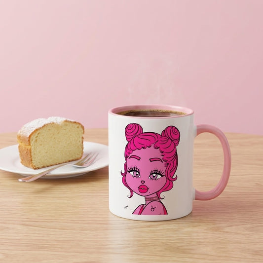 A white ceramic coffee mug with a pink handle and pink interior, featuring a cartoon illustration of a girl with pink hair. It sits on a light wood table next to a slice of cake on a white plate, against a solid pink background.