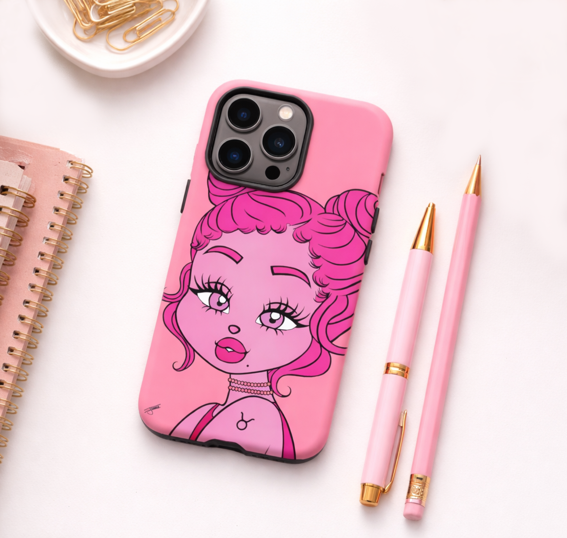 Phone case with a Taurus character design on a white surface with pens and a notebook.