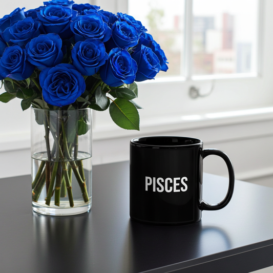 Black mug labeled 'PISCES' next to a vase of blue roses on a reflective surface.