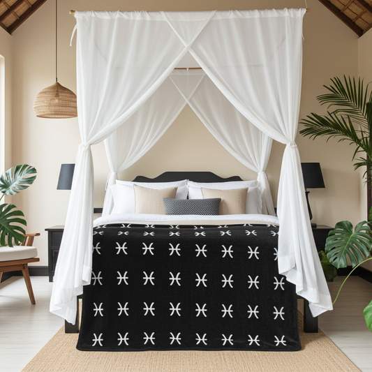Bed with black and white Pisces patterned bedding in a bedroom setting with white curtains and plants.