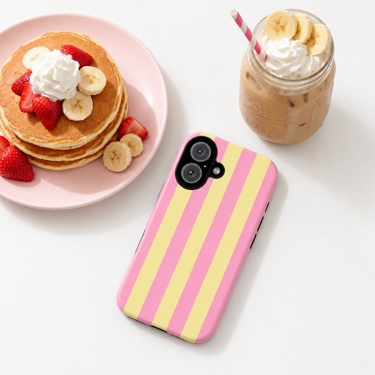 A pink and yellow vertically striped phone case with a camera cutout, displayed on a white surface next to a plate of pancakes and a mason jar iced coffee.