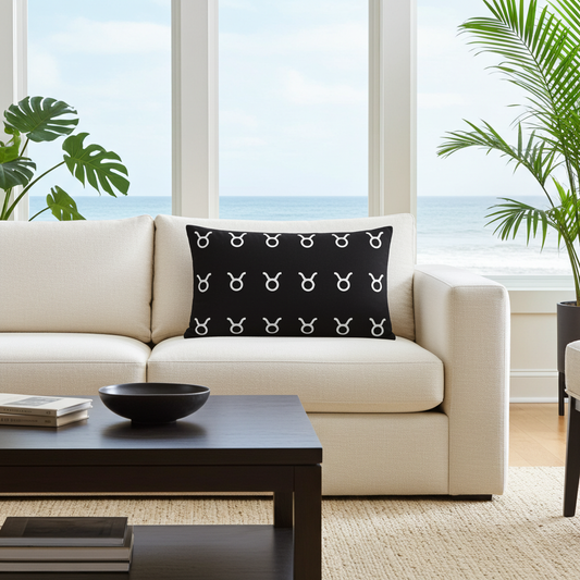 Beige sofa with a black pillow featuring white Taurus symbols in a living room with large windows and plants.